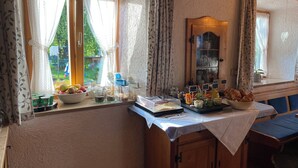 A breakfast setup with a variety of food items and condiments on a table near a window with curtains. - Apartment 2 with balcony, up to 2 pers. (Rottau)