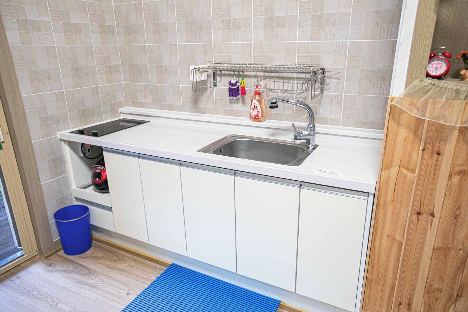 A kitchen with a double sink, a stainless steel faucet, a drying rack, and a blue mat on the floor.