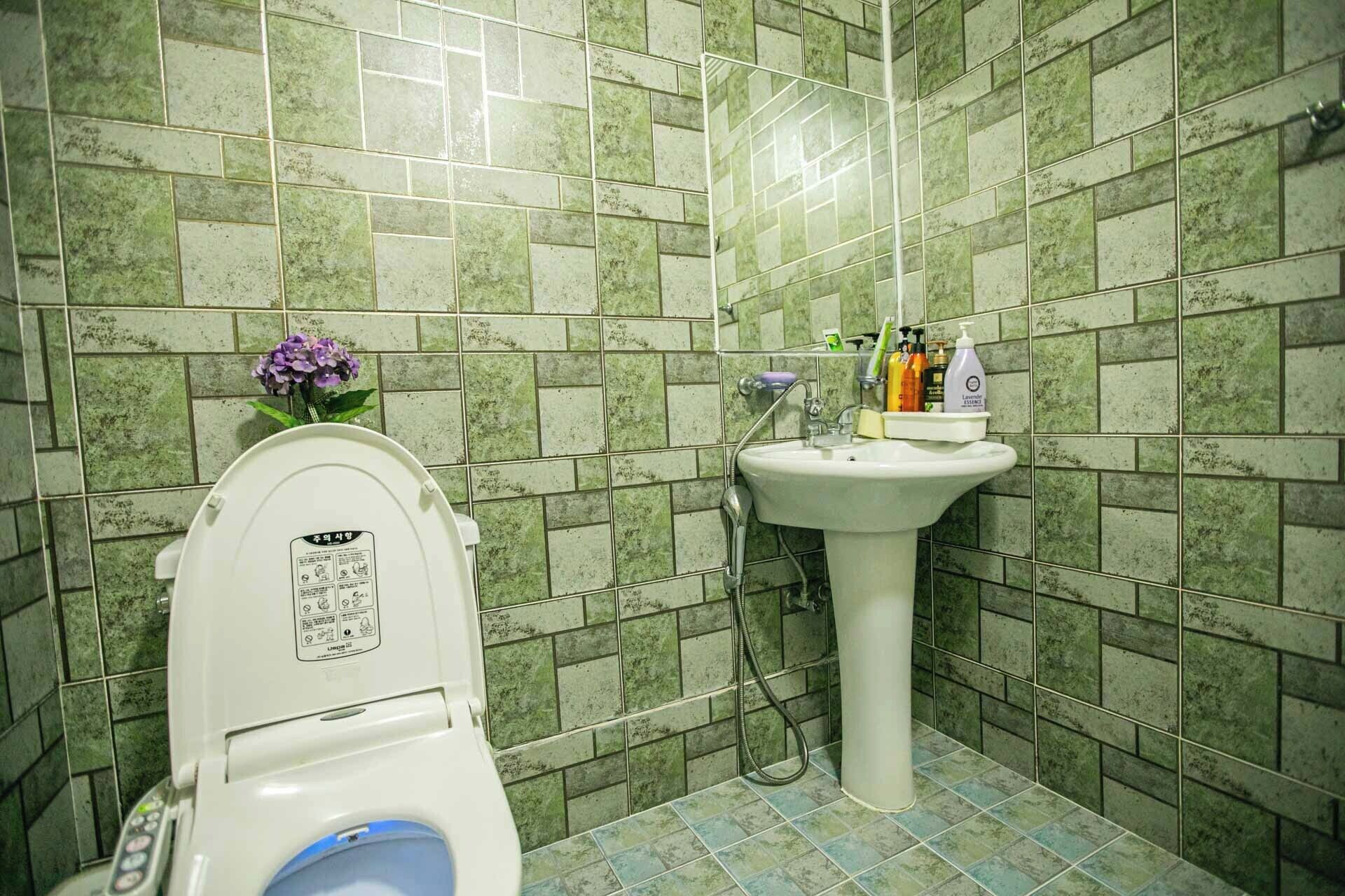 A bathroom with a toilet, sink, and green tiled walls.