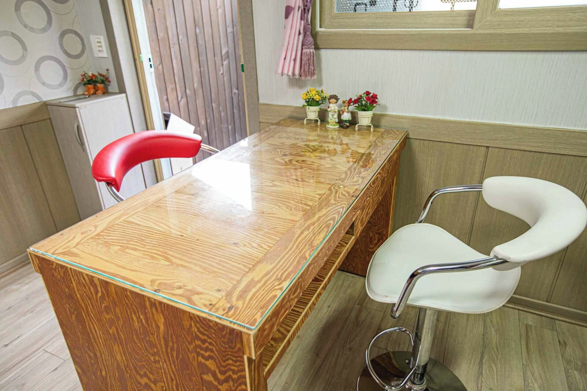 A wooden dining table with a glass top, a red chair, and a white chair with a curved backrest.