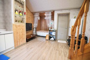 Una habitación con una cama, televisión, ventilador, microondas y un armario de madera.