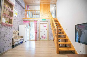 Un interior de varios niveles con una escalera de madera, un sofá, un refrigerador y un televisor.