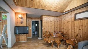 A wooden-paneled room with a TV, a dining table with chairs, and a sofa. - Jirisan 1 Night 2 Days Pension (Gurye)