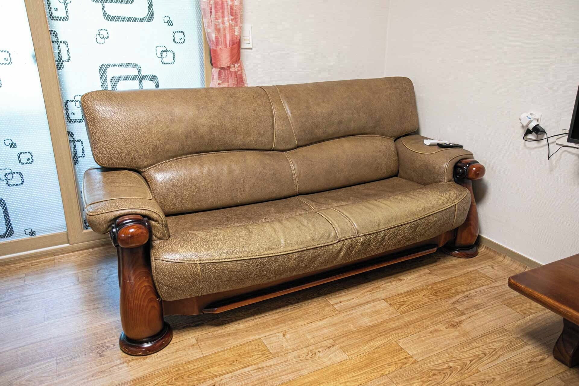 Un sofá de cuero marrón con patas de madera en una habitación con suelo de madera y persiana con estampado.