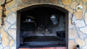 Un horno de piedra con una rejilla metálica, una campana colgante y un cartel que anuncia la disponibilidad de cerveza.