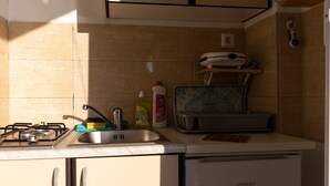 Una cocina pequeña con estufa a gas, lavamanos y un refrigerador compacto.