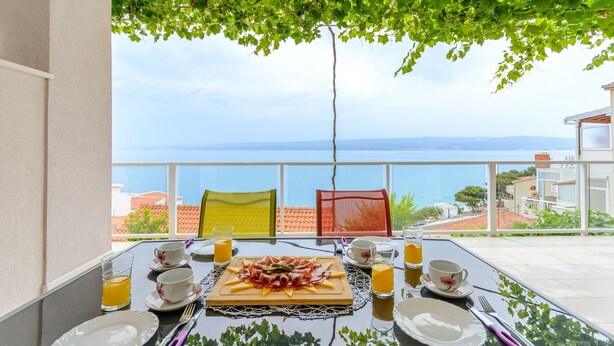 A table set for breakfast with a view of the sea, a pergola with green leaves, and colorful chairs. - Apartments Hope (Dugi Rat) - Standard One-Bedroom Apartment with Terrace and Sea View (A3) (Dugi Rat)