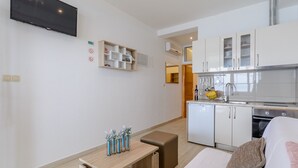 A modern hotel room with a kitchenette, a TV mounted on the wall, a small table with decorative vases, and a cozy seating area. - Apartments Hope (Dugi Rat) - Standard One-Bedroom Apartment with Terrace and Sea View (A3) (Dugi Rat)