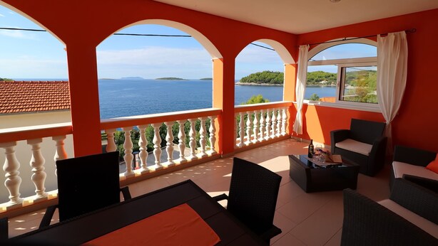 Un balcon donnant sur la mer et une île lointaine, aménagé avec des chaises et une table aux couleurs noir et blanc.