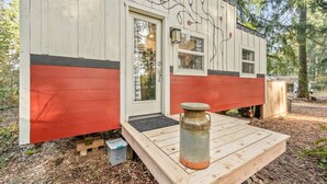 Une petite cabane à l’extérieur rouge et blanc, dotée d’une terrasse en bois et d’un conteneur métallique sur la terrasse.