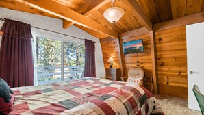 Un dormitorio con una cama grande, vigas de madera en el techo, una ventana con cortinas, un cuadro en la pared y una puerta.