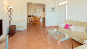 Un salon avec un canapé, une table basse en verre et un téléviseur. On aperçoit à l’arrière-plan un coin repas avec une table et des chaises.