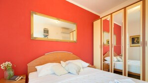Une chambre d’hôtel avec un grand lit, une tête de lit en bois, une table de chevet avec un téléphone et un livre, un miroir au-dessus du lit et une armoire avec un miroir.