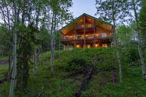 A large log cabin with a two-story balcony, surrounded by dense forest. - Nestled in the mountains, 20 min ➡️ Yellowstone,  AC, WI-FI, Large Porch 🏕️ (Island Park)