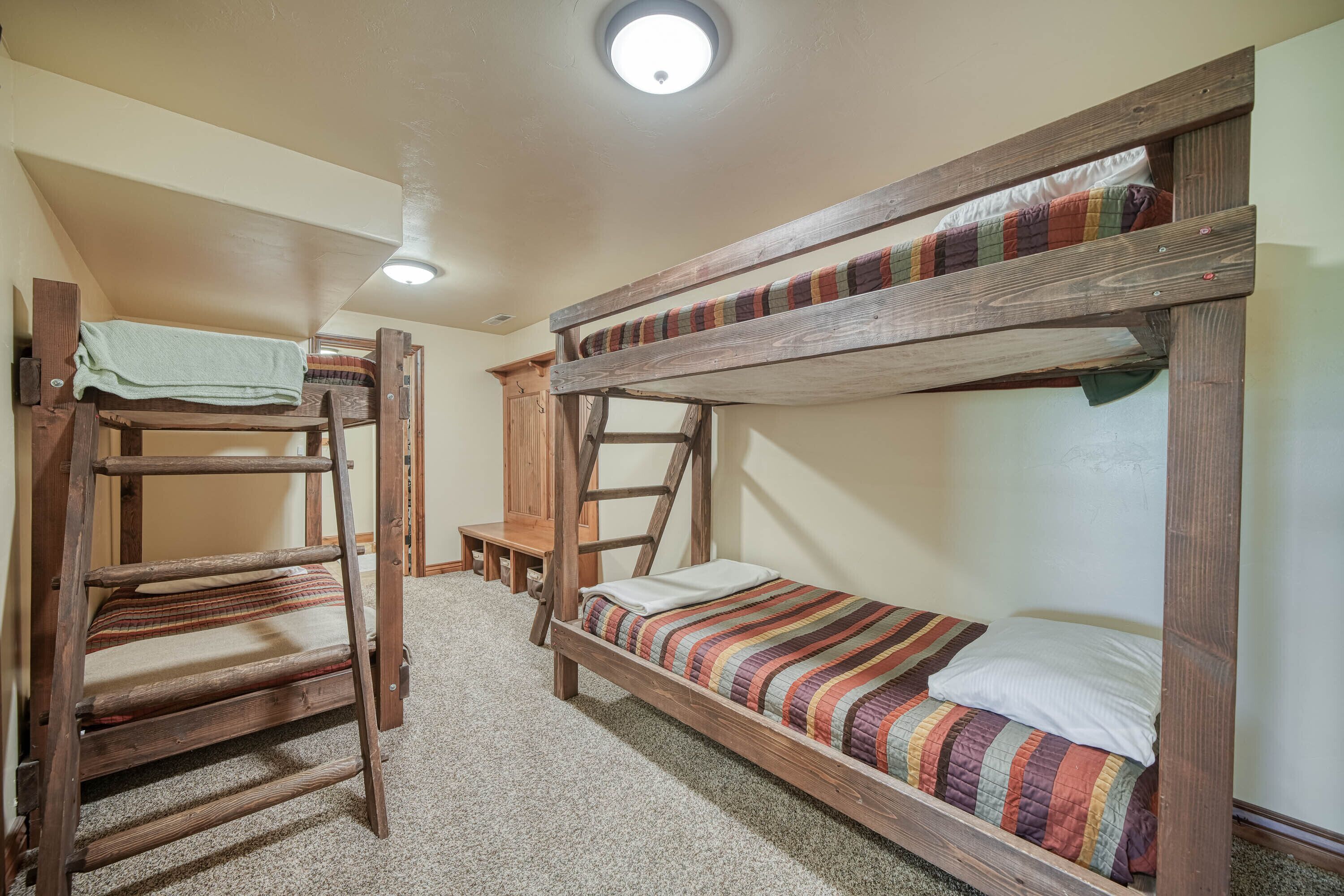 A bunk bed room with a wooden ladder, a small table, and a ceiling light.