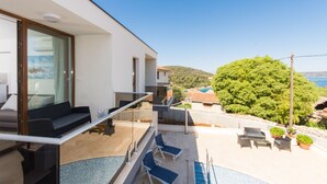 Un balcón moderno con piscina, mobiliario exterior y vistas al mar y a las colinas.