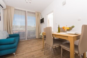 A modern living room with a teal sofa, a wooden dining table with chairs, a TV mounted on the wall, and a balcony with a view. - Villa LA-Comfort One Bedroom Apartment with Sea View Terrace 1 (Drvenik Veliki)