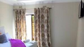 Ein Schlafzimmer mit Bett, Vorhängen, Fenster und Nachttisch.