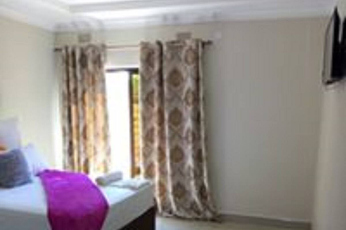 A bedroom with a bed, curtains, a window, and a bedside table.