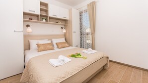 Una cama bien tendida con un edredón color beige, una mesita de noche con lámpara y una ventana con cortinas.