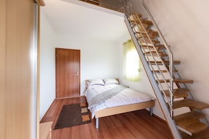 Un dormitorio con cama y puerta de madera, una escalera y una ventana con cortinas.