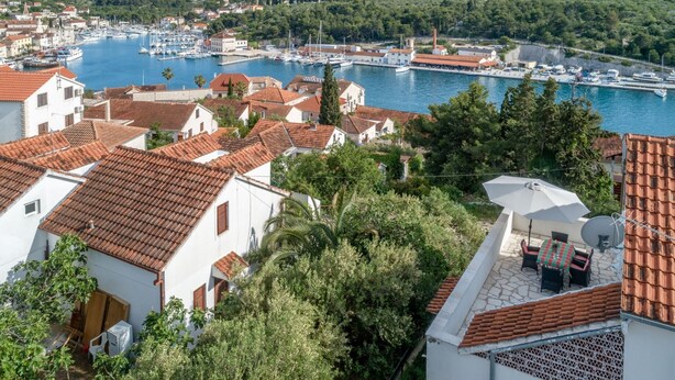 Uma cidade costeira com edifícios de telhados em terracota, uma marina com barcos e vegetação exuberante.