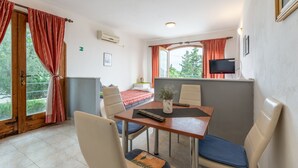 Quarto com uma cama, uma mesa de jantar com cadeiras, uma televisão e uma janela com cortinas.
