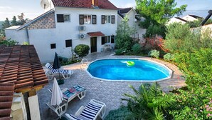 Uma casa com piscina, rodeada por vegetação e um terraço com pavimento cerâmico.