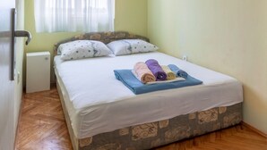 Quarto com cama, janela com cortinas leves, radiador e piso de madeira.