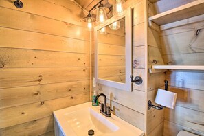 Ein Badezimmer mit Holzvertäfelung, einem weißen Waschbecken, einem Spiegel und einem Handtuchhalter.