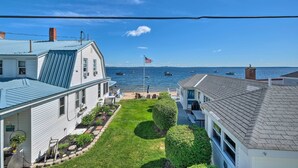 A residential area with a view of the sea, featuring houses with blue roofs, a lawn, and a flag. - Sebago Lake Haven: Water Views, Steps to Shoreline (Sebago)