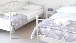 Een slaapkamer met twee bedden, een klein nachtkastje en een witte muur.