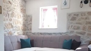 Een woonkamer met een stenen muur, een bank, een bijzettafeltje en een raam met gordijnen.