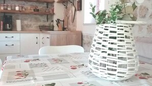 Een keuken met een eettafel, een hanglamp en een wandplank met keukengerei.