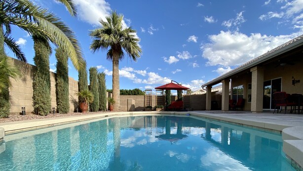 A clear swimming pool with a red umbrella, surrounded by palm trees and a covered patio area. - Your perfect AZ getaway with putting green and optional HEATED private pool! (Chandler)