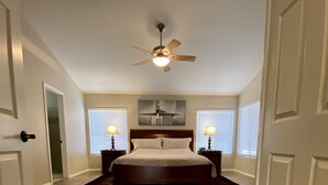 A bedroom with a bed, a ceiling fan, two bedside lamps, and a window with blinds. - Your perfect AZ getaway with putting green and optional HEATED private pool! (Chandler)