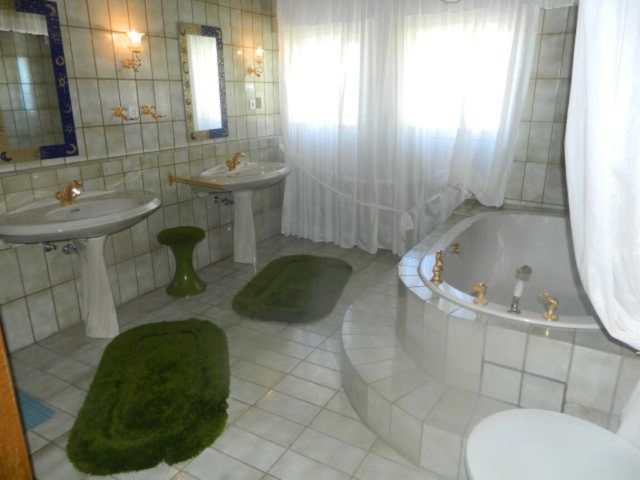 A bathroom with a bathtub, two sinks, a toilet, and a green rug.