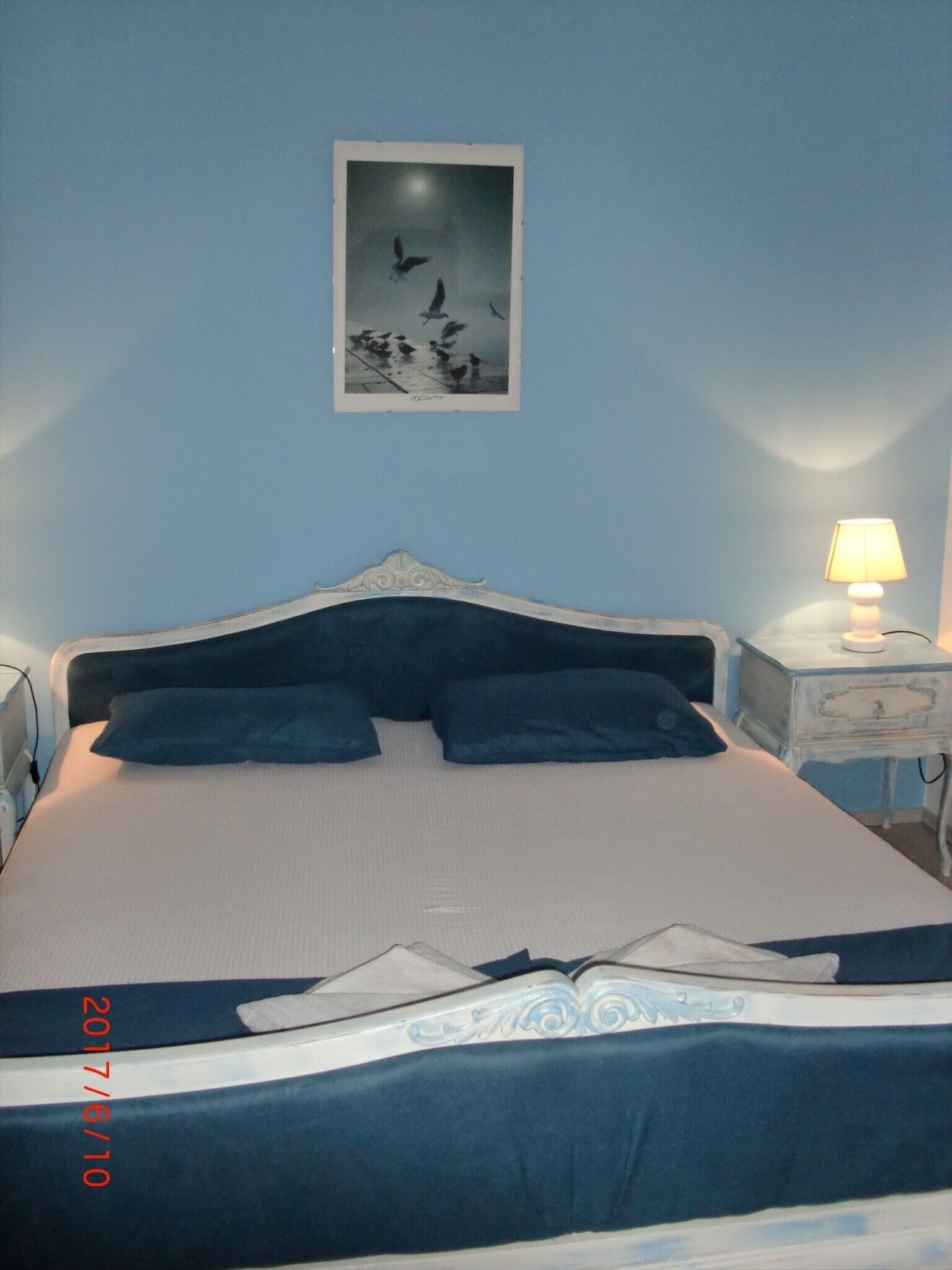 A neatly made bed with a headboard, a bedside table with a lamp, and a framed picture on the wall.