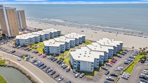 Een hotel aan het strand met meerlaags gebouwen, een parkeerplaats en een strand op de achtergrond.