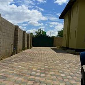 Un patio empedrado con piso de ladrillo, rodeado de muros y un edificio con puerta verde.