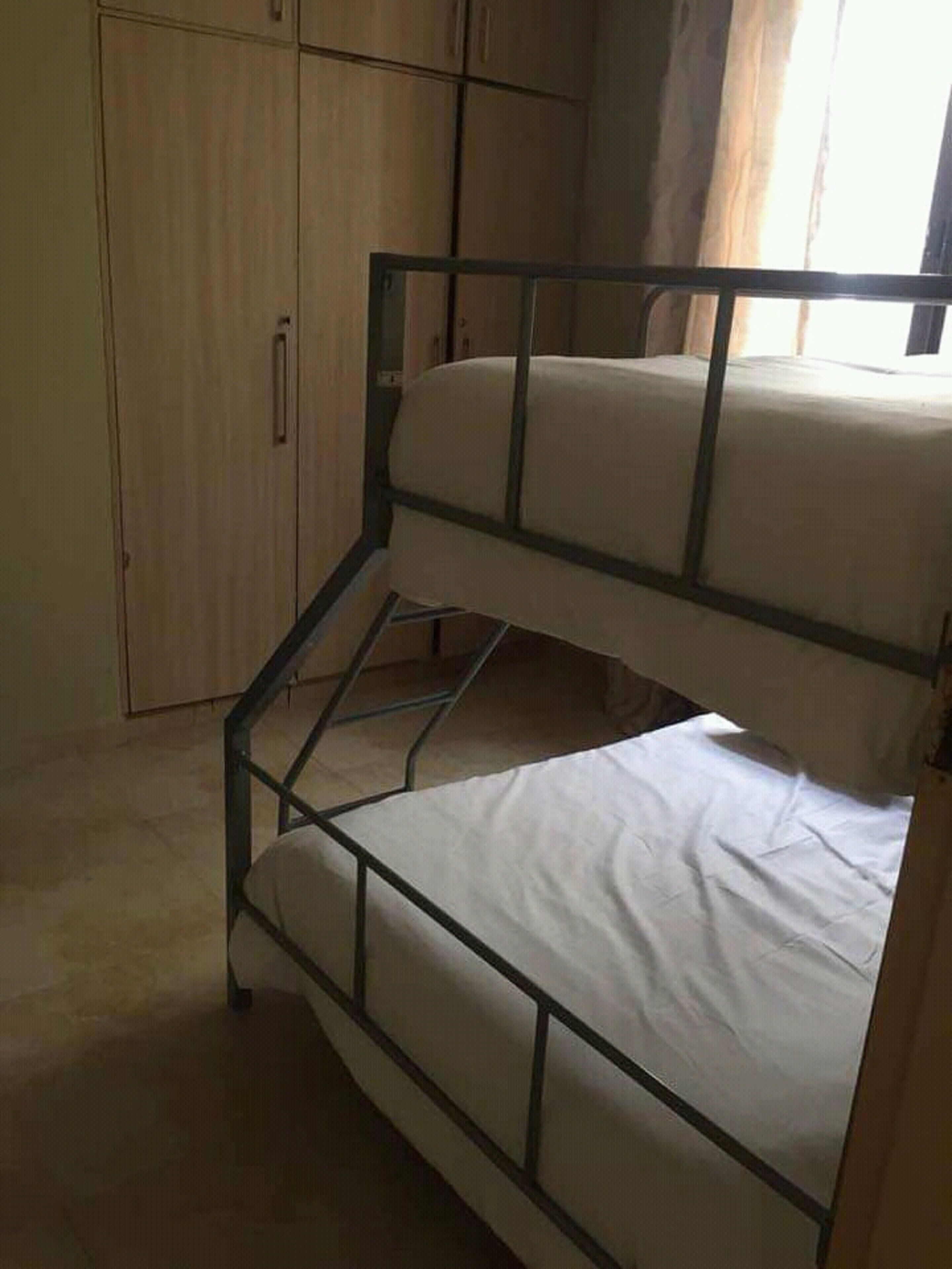 Un lit superposé avec un lit en bas et un lit simple, une armoire en bois et une fenêtre avec des rideaux.