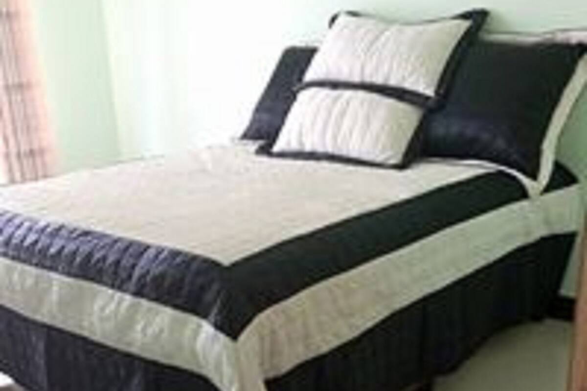 A bed with a black and white bedspread, a white pillow, and a dark pillow.