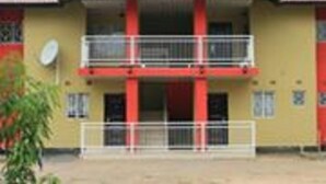 Un edificio de dos pisos con fachada roja y amarilla, una antena parabólica y una entrada con portón.