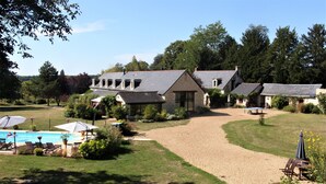 Une grande maison avec une piscine, entourée d’une pelouse bien entretenue et d’arbres.