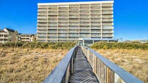 A long wooden boardwalk leading to a large, multi-story building with balconies. - 🏖️Pelican Watch 302: Oceanfront | Indoor + Outdoor Pool | Hot Tub🏖️ (Carolina Beach)