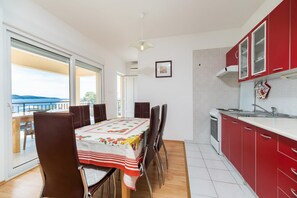 Uma área de refeições com uma mesa posta para quatro pessoas, uma cozinha com armários vermelhos e uma varanda com vista.