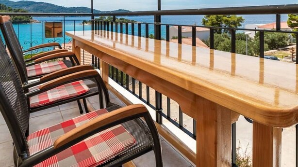 Un balcón con mesa y sillas de madera, con vistas a una masa de agua y colinas distantes.