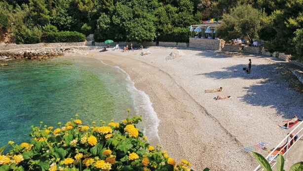 A beach with clear water, people sunbathing, and a stone wall.