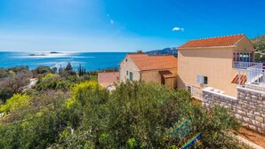 A coastal property with a view of the sea, stone buildings, and lush greenery.