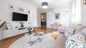 A modern living room with a flat-screen TV, a round coffee table, a sofa, and a dining area with a table and chairs.